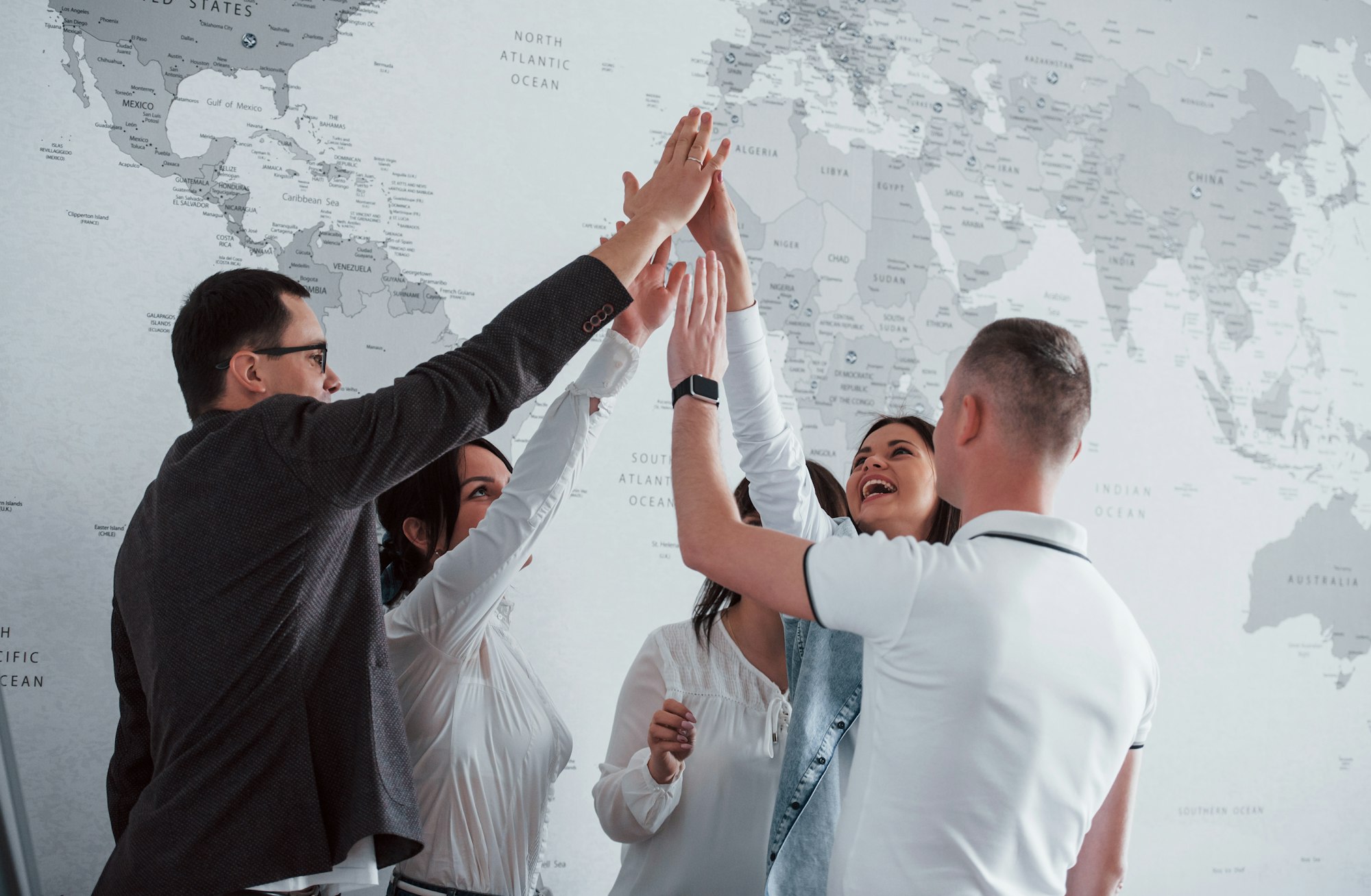 Celebrating success. Team of freelancers standing against wall with map of the world on it