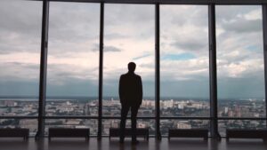 Rear view of man in formal suites who stand in front of panoramic window with city view. a man