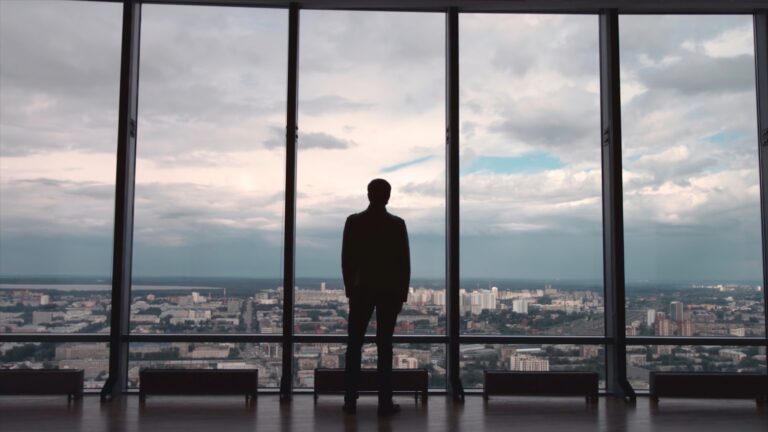 Rear view of man in formal suites who stand in front of panoramic window with city view. a man