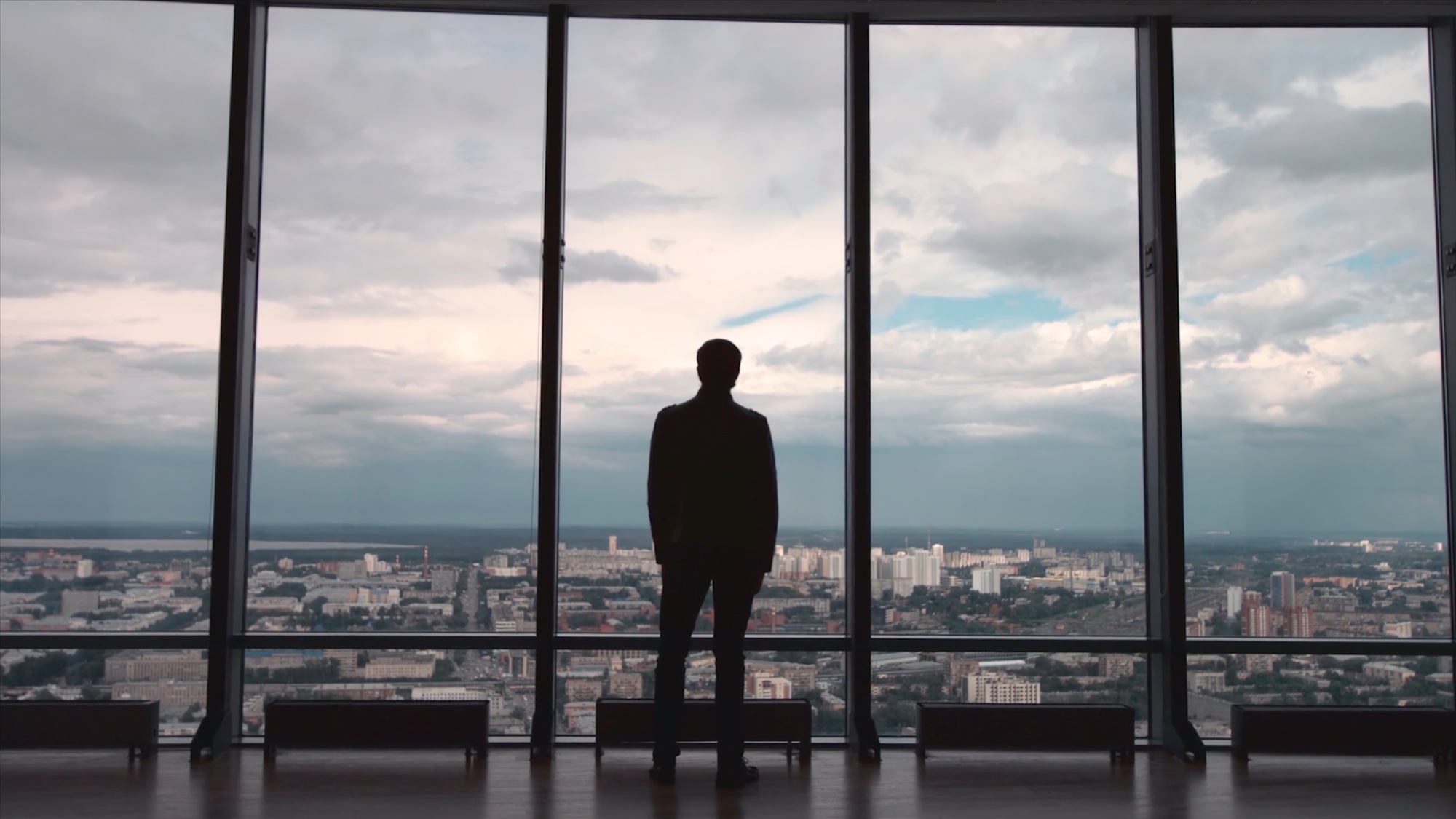 Rear view of man in formal suites who stand in front of panoramic window with city view. a man